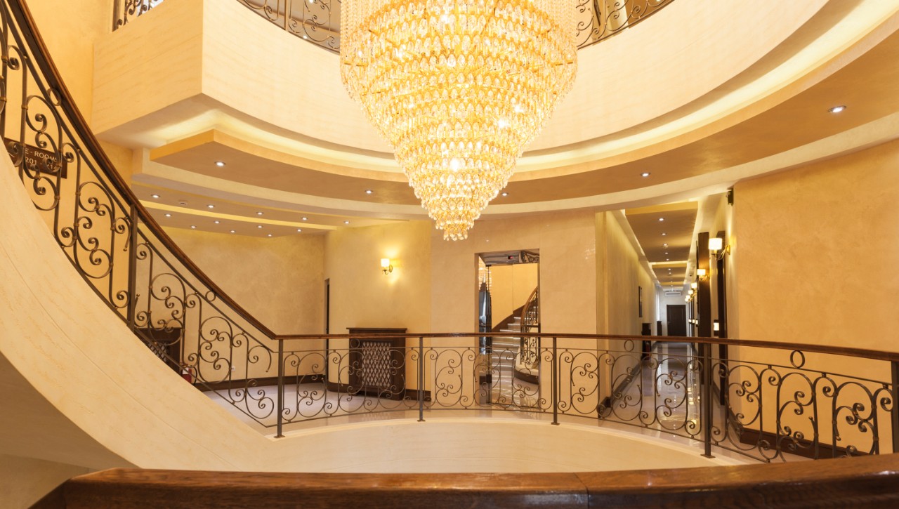 A large crystal chandelier shines above a winding staircase in a hotel.